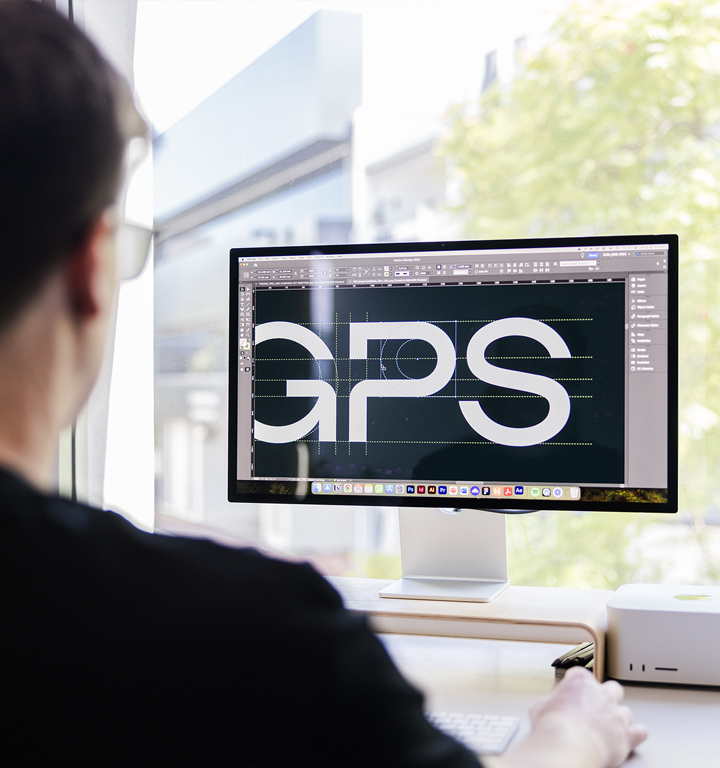 A creative professional at Four Stripes Design Agency in Subiaco meticulously perfects a bold 'GPS' logotype on a computer screen, highlighting the agency's detail-oriented approach to brand identity development.