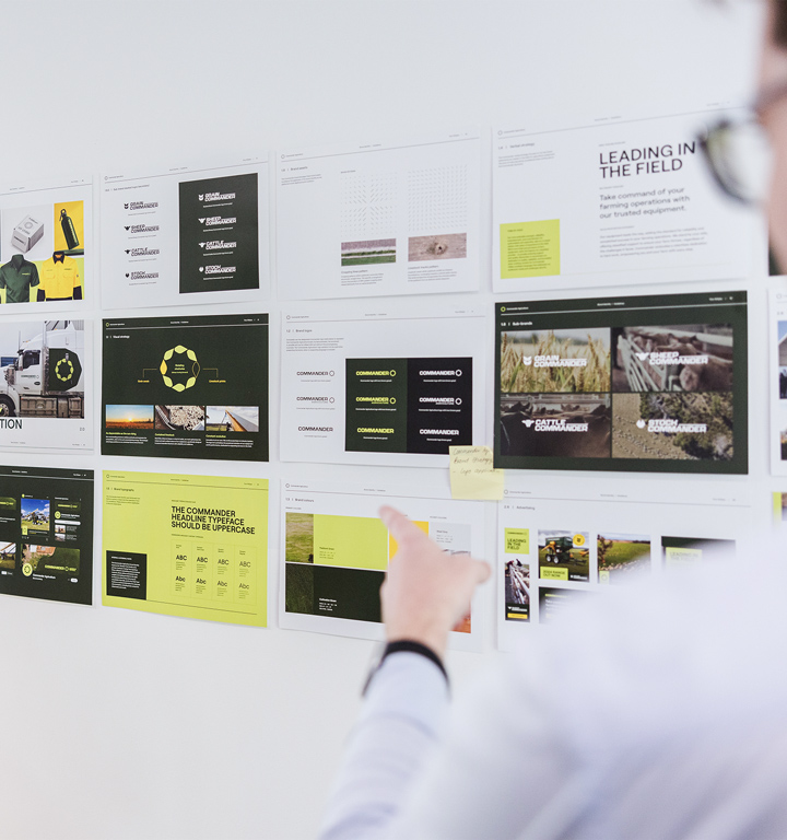 A design professional at Four Stripes Design Agency points to specific elements in a series of print layouts on the wall, each depicting different aspects of a cohesive branding package, underscoring the agency's culture of detail-oriented critique and excellence.