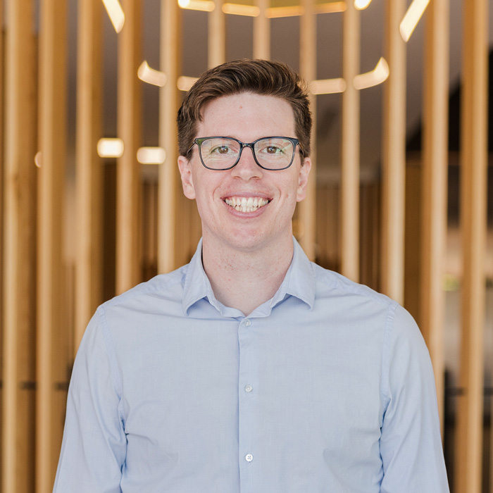 Portrait of Cain, a dedicated professional at Four Stripes Design Agency, with a focused gaze that reflects the agency's commitment to quality in brand identity design. The wooden slat background adds a touch of warmth to the modern Subiaco office setting.