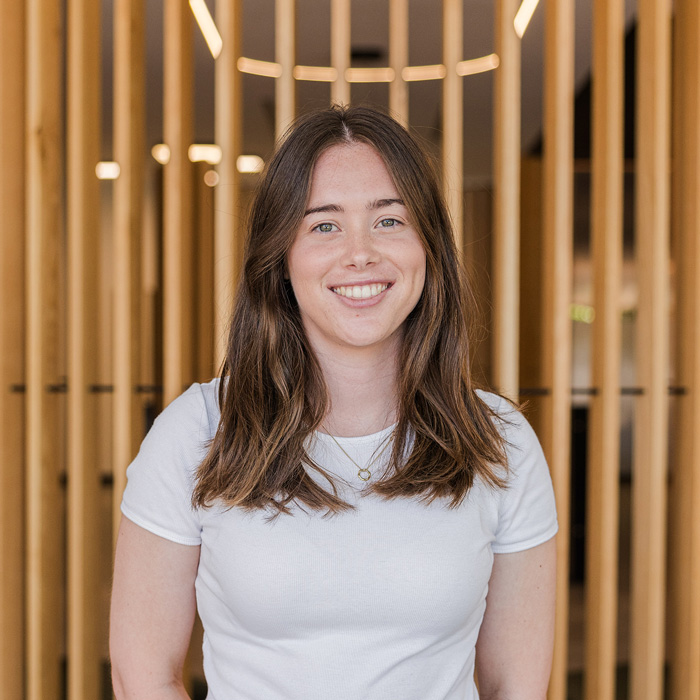 Portrait of Sarah, a team member at Four Stripes Design Agency, smiling confidently in the office, with a creative wooden slat background reflecting the warm and inviting culture of the agency located in Subiaco.