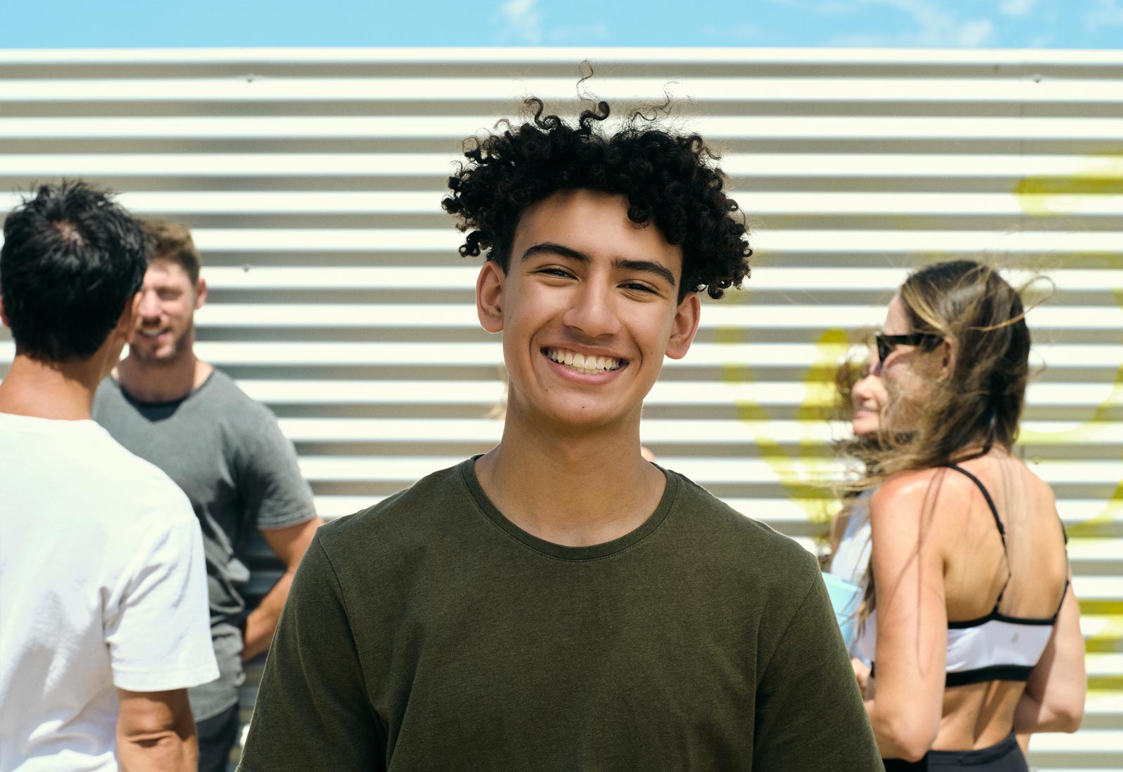 A smiling teenager stands at the forefront of the photo, men and women stand in the background in front of a Push-Up Challenge branded wall