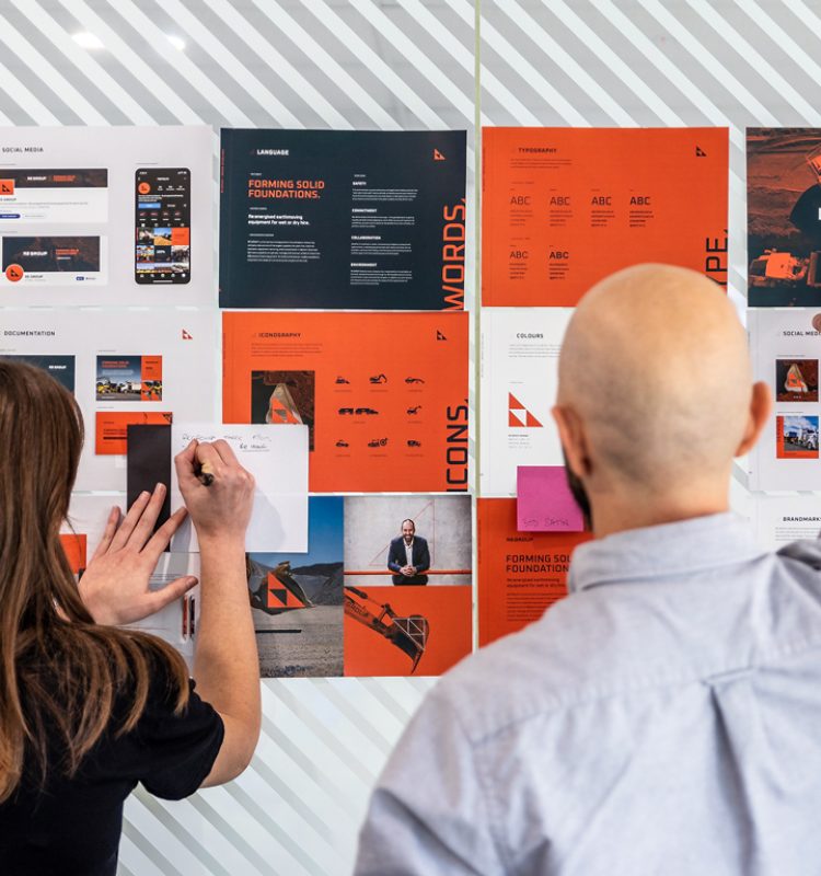 Members of the Four Stripes Design Agency team actively engage with a wall of branding materials, contributing to a vibrant visual strategy discussion, in an office space that reflects a culture of energetic creativity and resourcefulness.